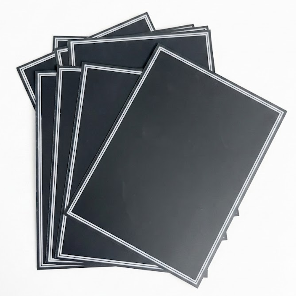 Paquet de dix ardoisines noires rectangulaires avec bordure blanche empilées en éventail sur fond blanc