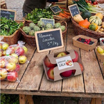 Barquette carton kraft contenant des pommes Gala sur un étal de marché avec légumes et fruits frais