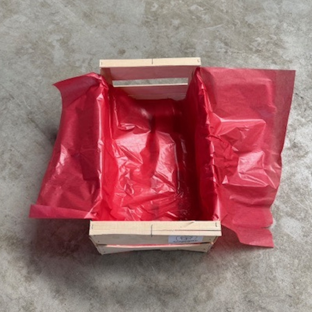 Papier Cristallose rouge 50x100cm en rame dans une caisse en bois ouverte sur sol béton
