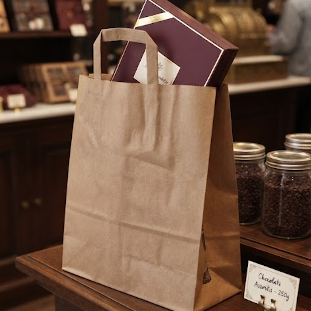Sac cabas kraft avec poignées plates contenant une boîte violette, posé sur un comptoir de boutique