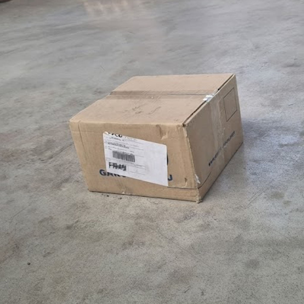 Carton de sachets en pointe modèle Times posé au sol, avec étiquette d'expédition visible