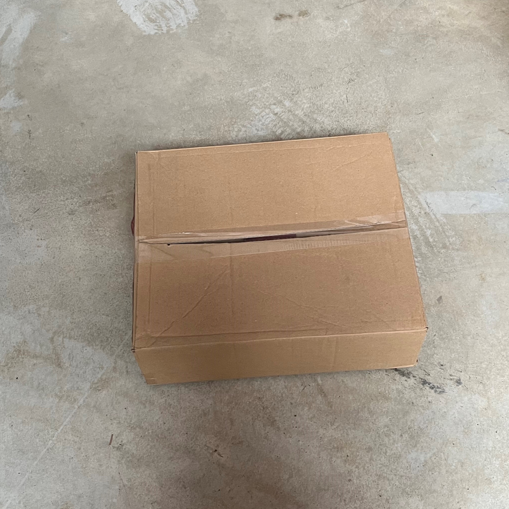 Carton d'emballage fermé contenant des sacs carottes 2kg impression rouge, posé sur sol béton