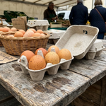 Boîte à œufs en carton moulé contenant 6 œufs bruns, posée ouverte sur table en bois de marché
